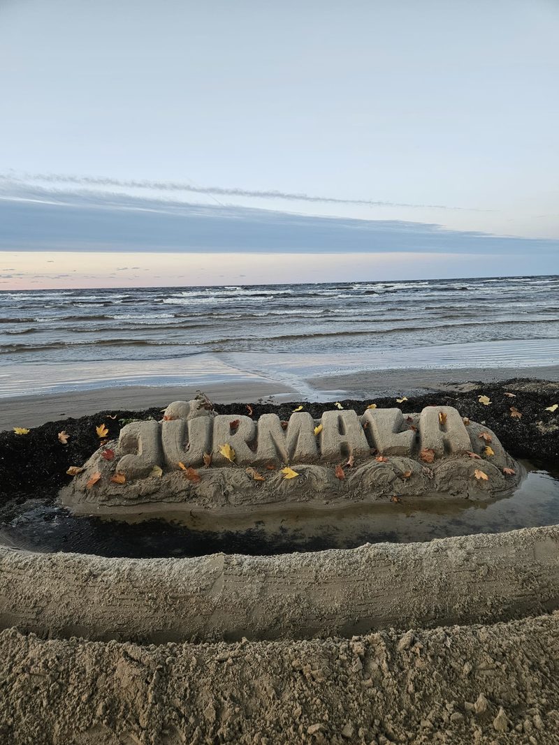 Smilšu skulptūra ar uzrakstu „Jūrmala” pludmalē krēslā